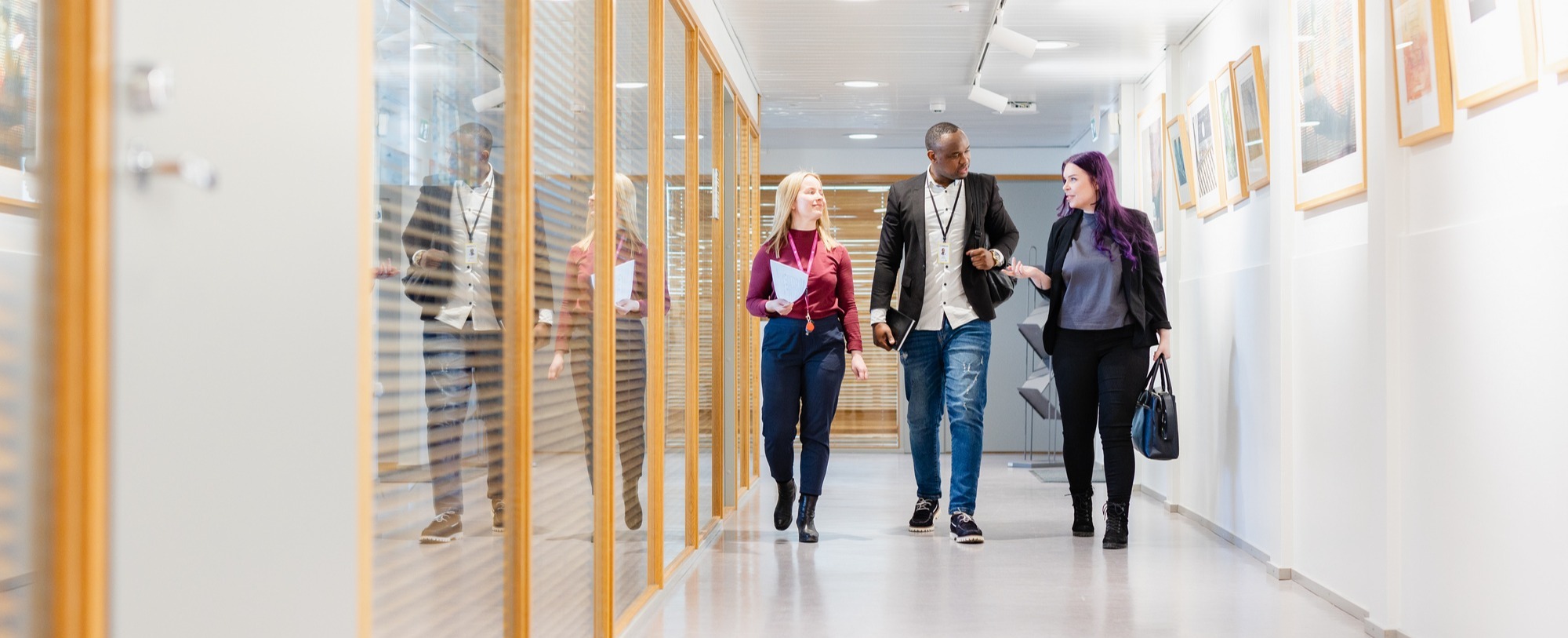 Kolme henkilöä kävelemässä toimiston käytävällä.