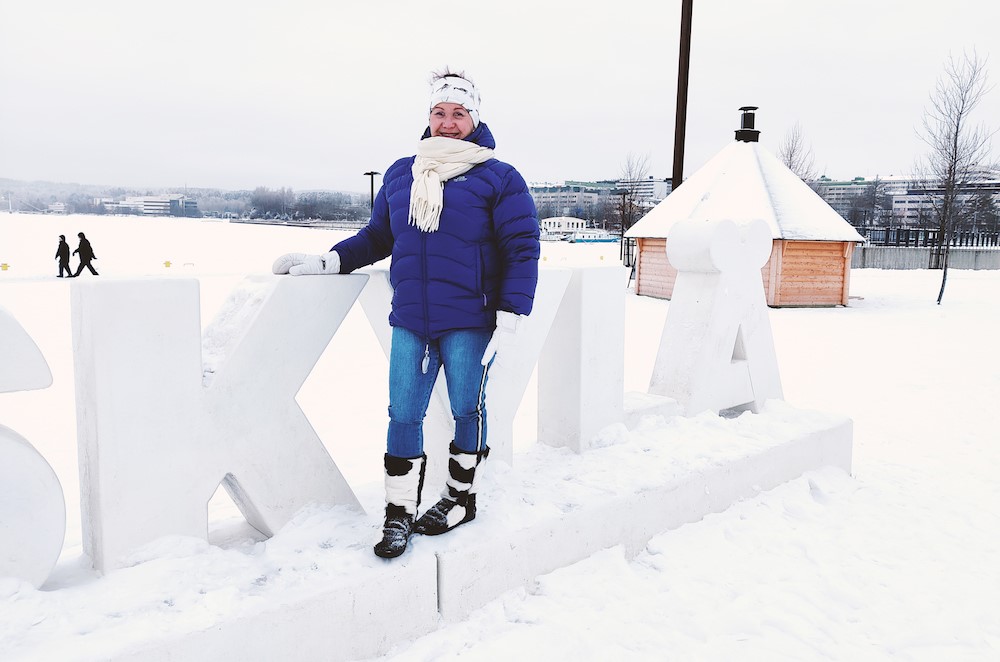 kuva 1: Mauree Hamilton seisoo kädet taskussa, lumisen järvimaiseman edessä. Kuva 2: Mauree Hamilton poseeraa Jyväskylä-kyltin päällä. Takana luminen kotamaisema.